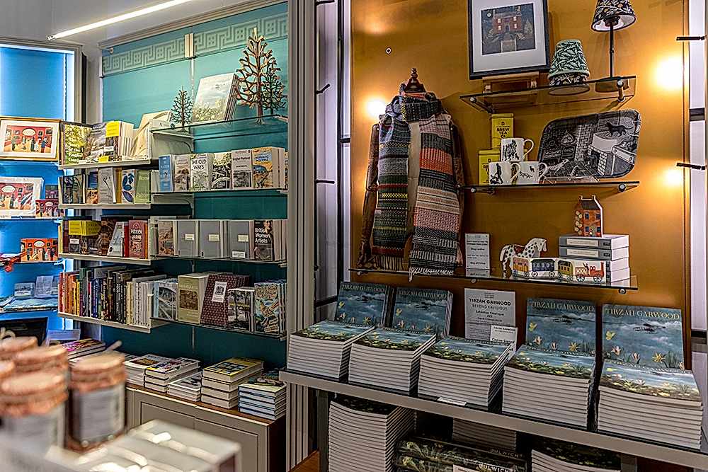 Photograph of a shop interior featuring books, scarfs, mugs and cards