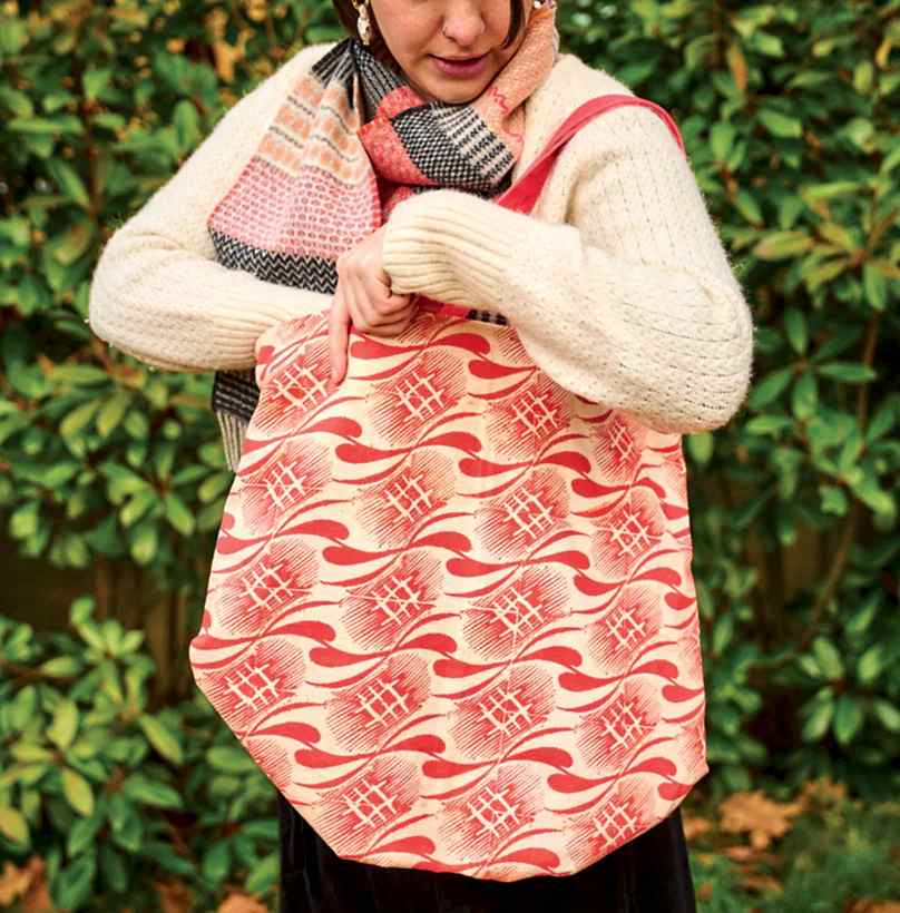 Photograph of a woman in white jumper with a red patterned tote bag on her shoulder