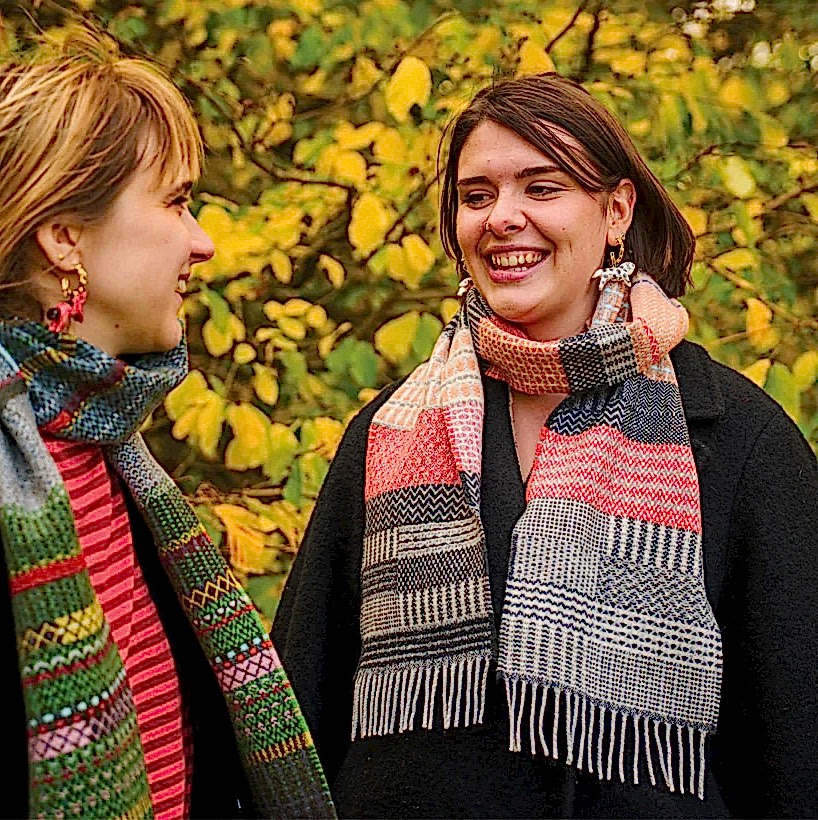 Photograph of two women wearing patterned scarfs looking at each other smiling